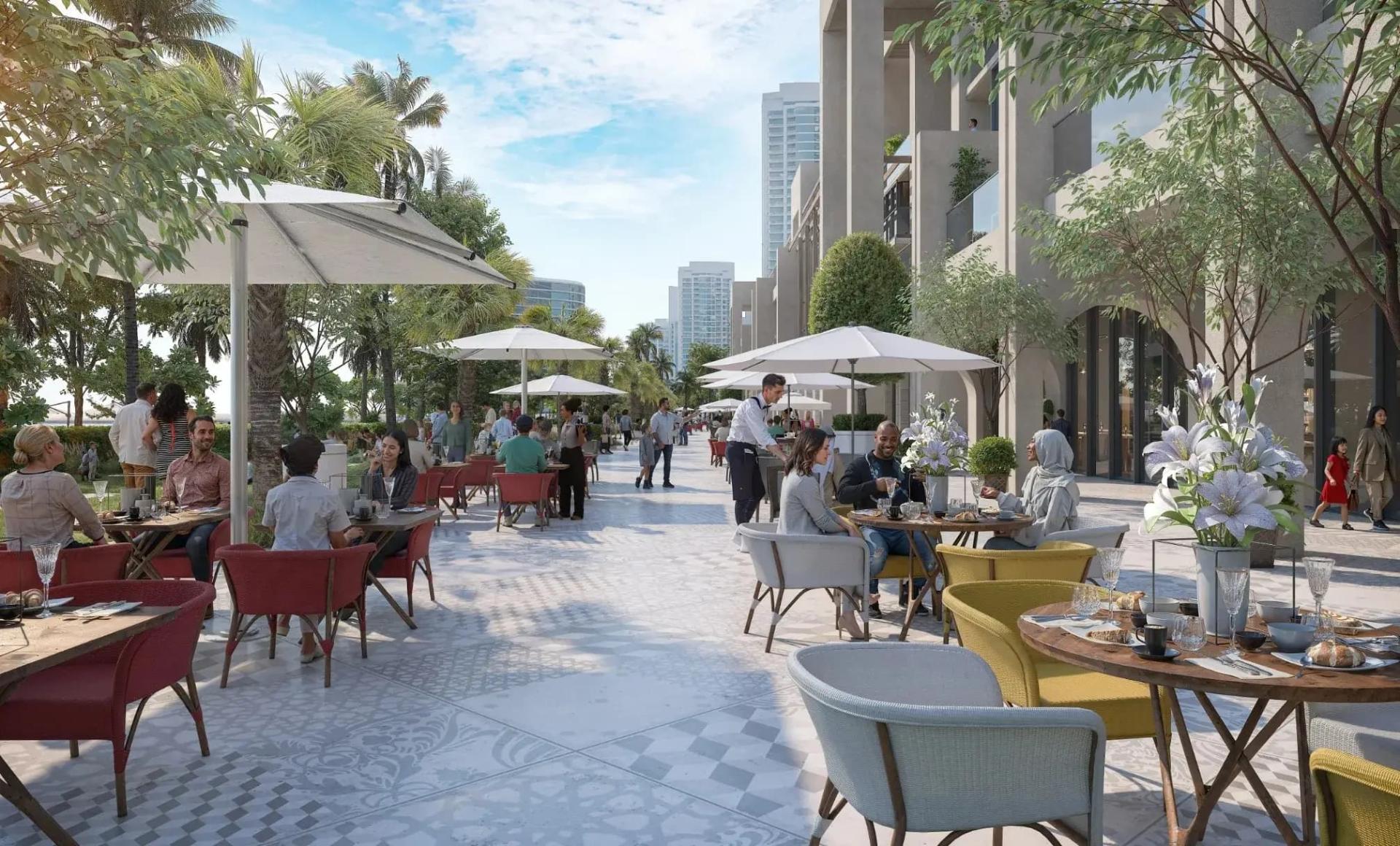 Sunlit waterfront promenade at Sobha Aquacrest with outdoor restaurants, white parasols and mature greenery